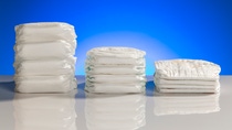 Three stacks of baby diapers with different diaper thickness on a table in front of a blue background. Three stacks of baby diapers with different diaper thickness on a table in front of a blue background.